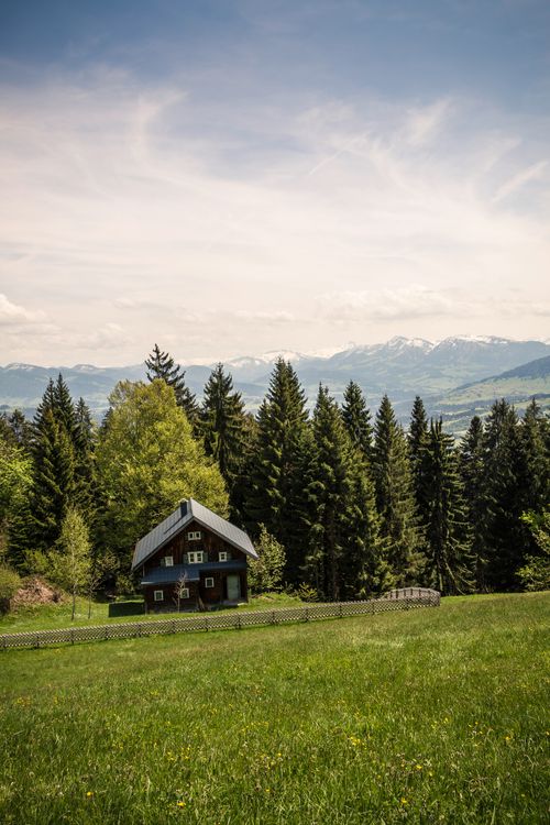 Free Scenic view of a countryside house surrounded by lush green trees and mountains under clear blue sky. Stock Photo