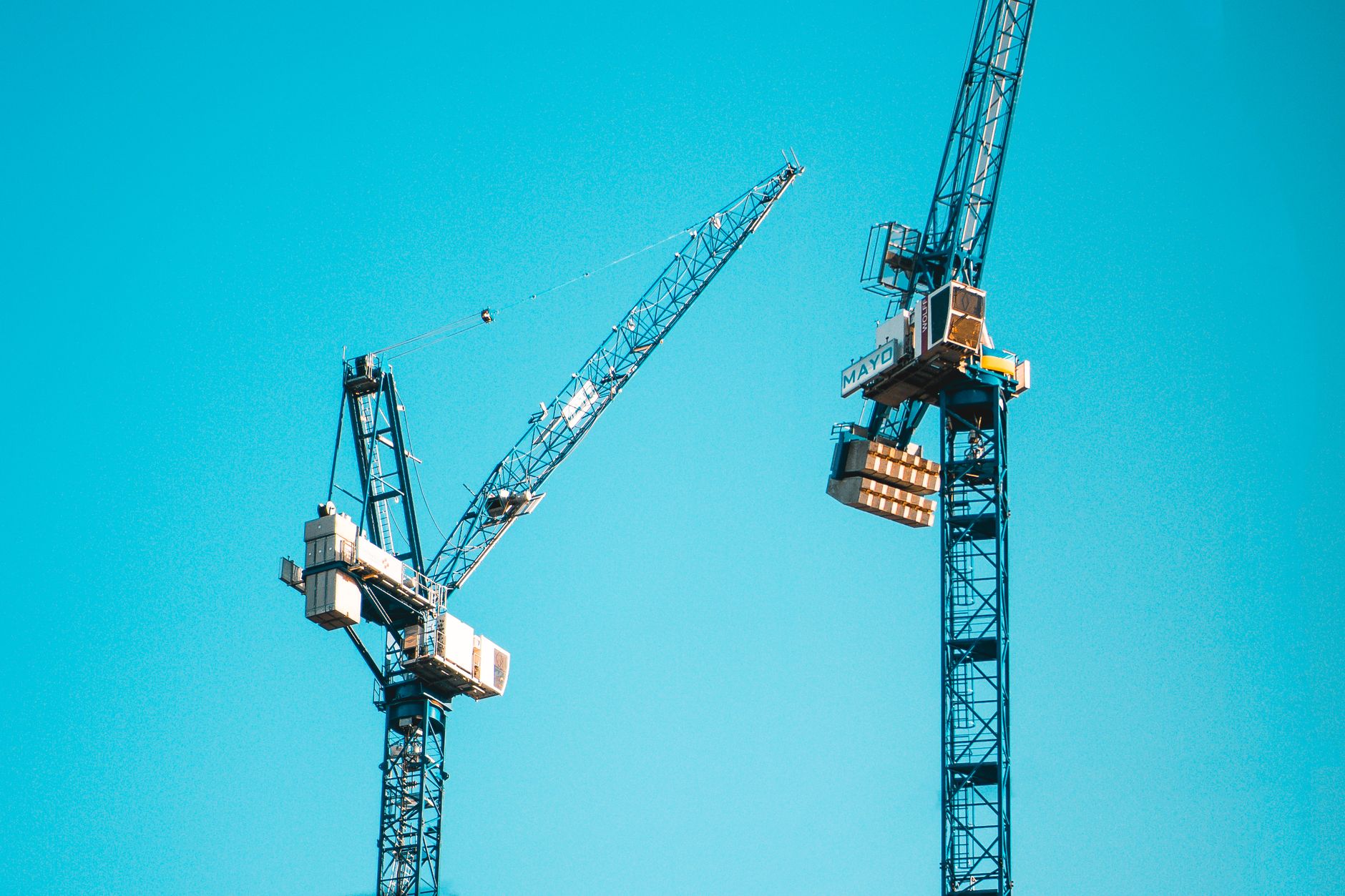 Two tower cranes dominate the skyline with a bright blue sky backdrop in Manchester.