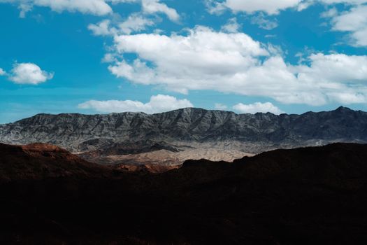 A stunning mountain landscape with eroded peaks against a bright blue sky and scattered clouds.