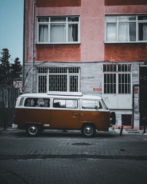 Free Classic retro van parked beside a pink residential building with metal railings on a paved road. Stock Photo