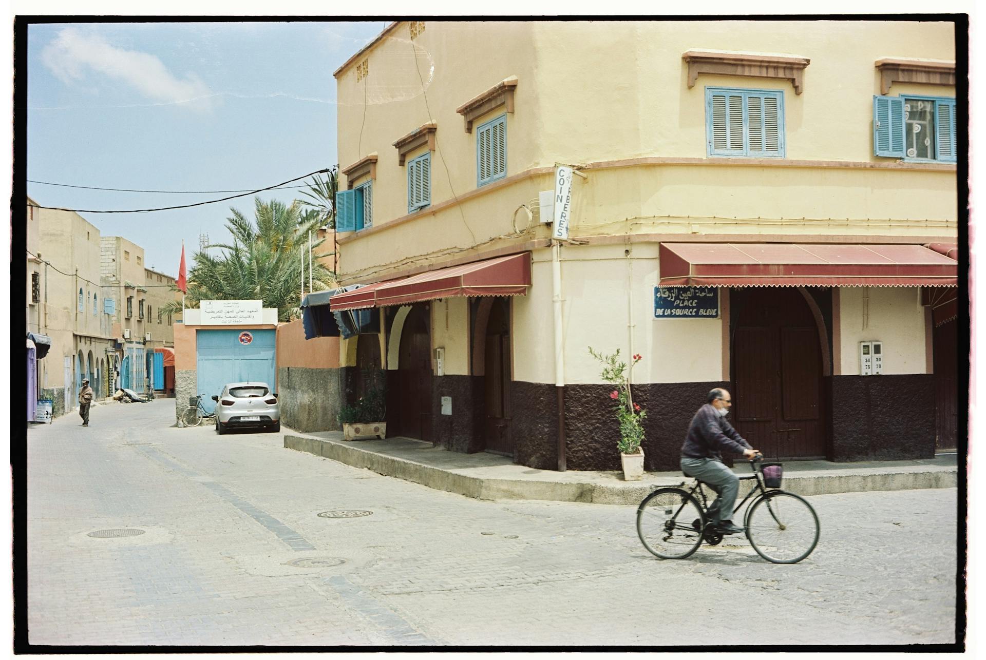 A cyclist rides past old buildings in a quiet Moroccan street.