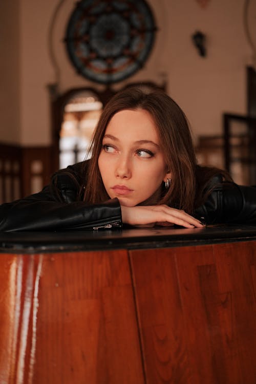 Woman in Leather Jacket Leaning on Wooden Table while Looking Afar 