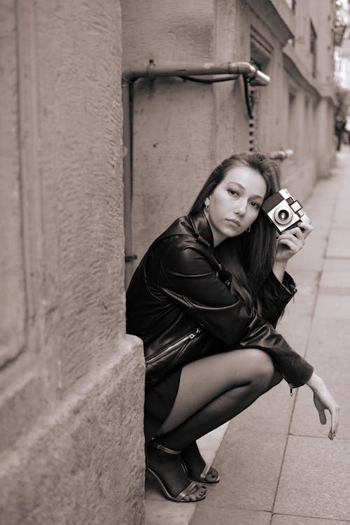 
A Grayscale of a Woman in Leather Jacket Holding a Camera
