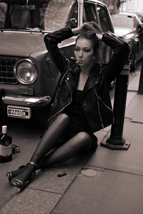 Sepia Toned Image of a Woman Wearing Leather Jacket and Tights Sitting on a Pavement