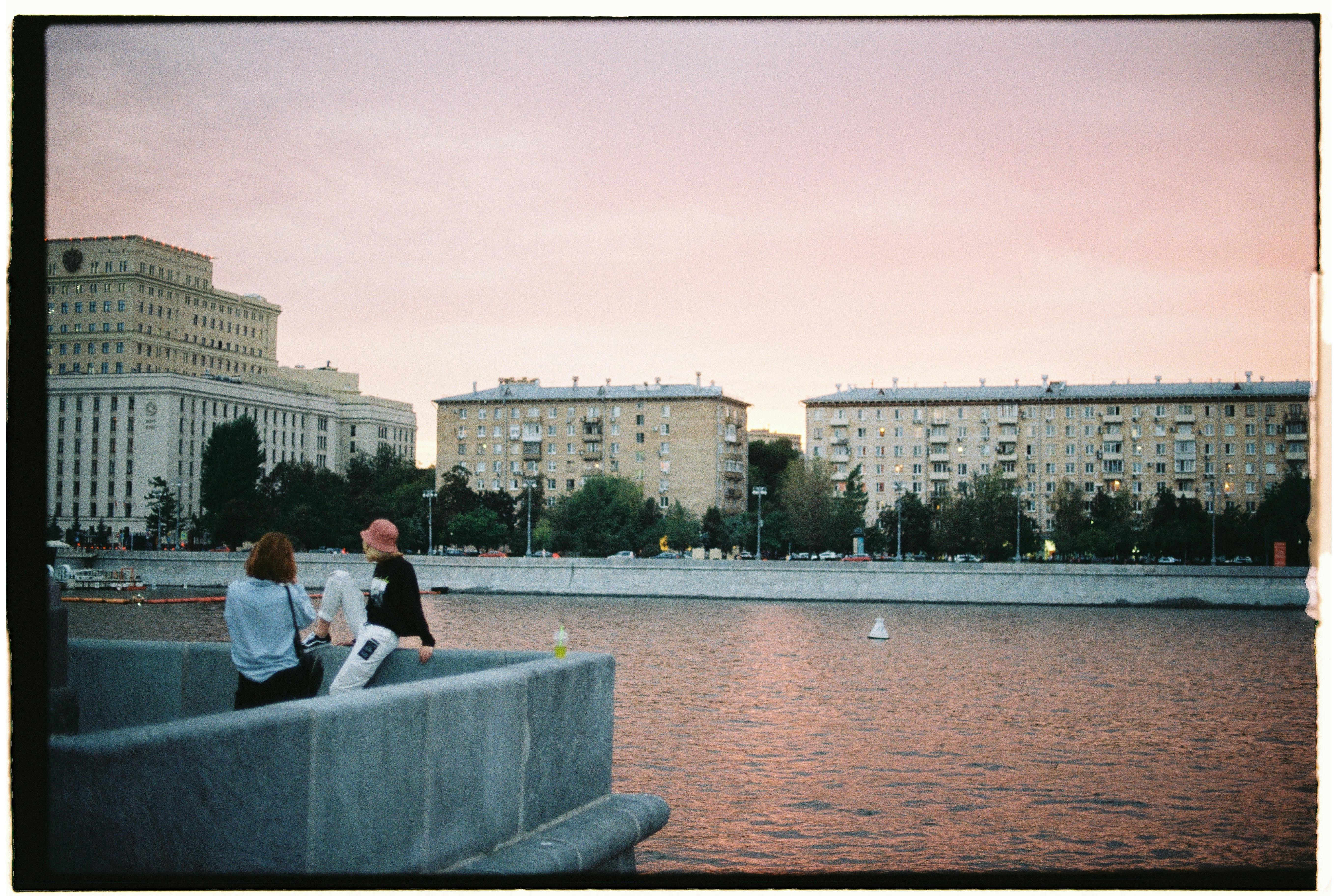 View of Moscow river at sunset with urban buildings and vibrant sky reflection.