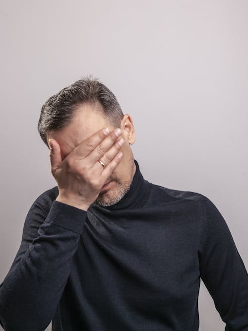 Man in Black Sweater Covering His Face with His Hand
