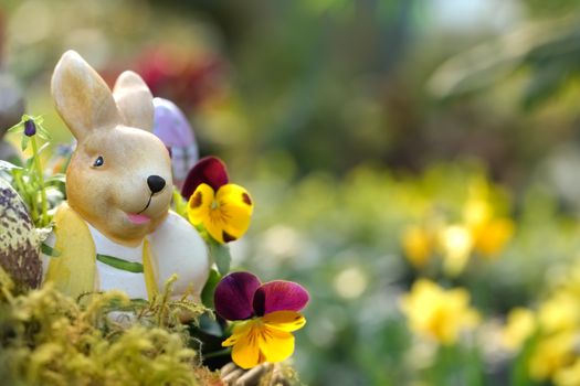 Charming Easter bunny sculpture amidst blooming pansies in a vibrant garden setting.