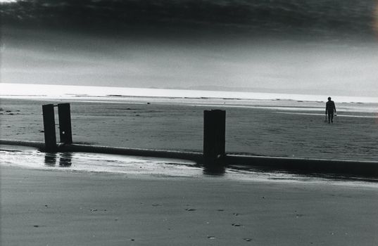 A tranquil black and white beach scene featuring a solitary figure walking along the seashore.