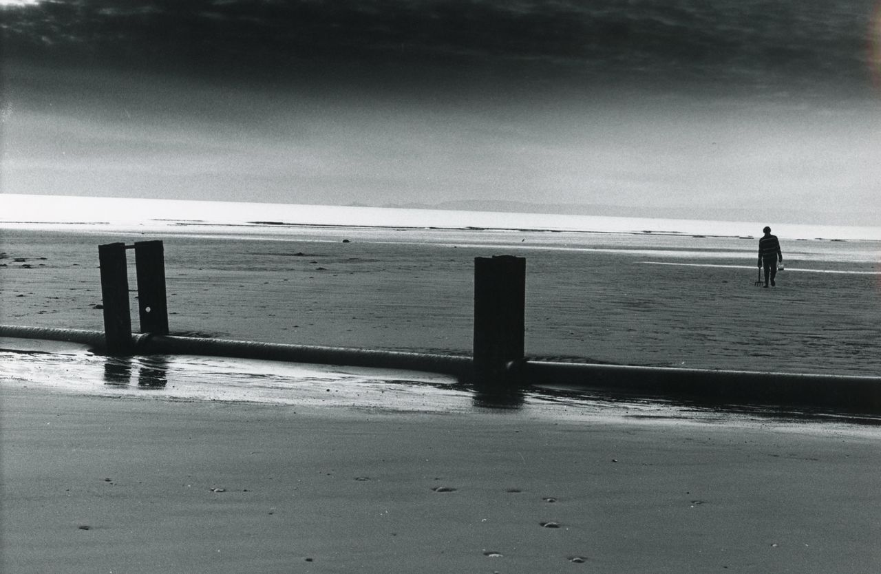 a tranquil black and white beach scene featuring a solitary figure wal