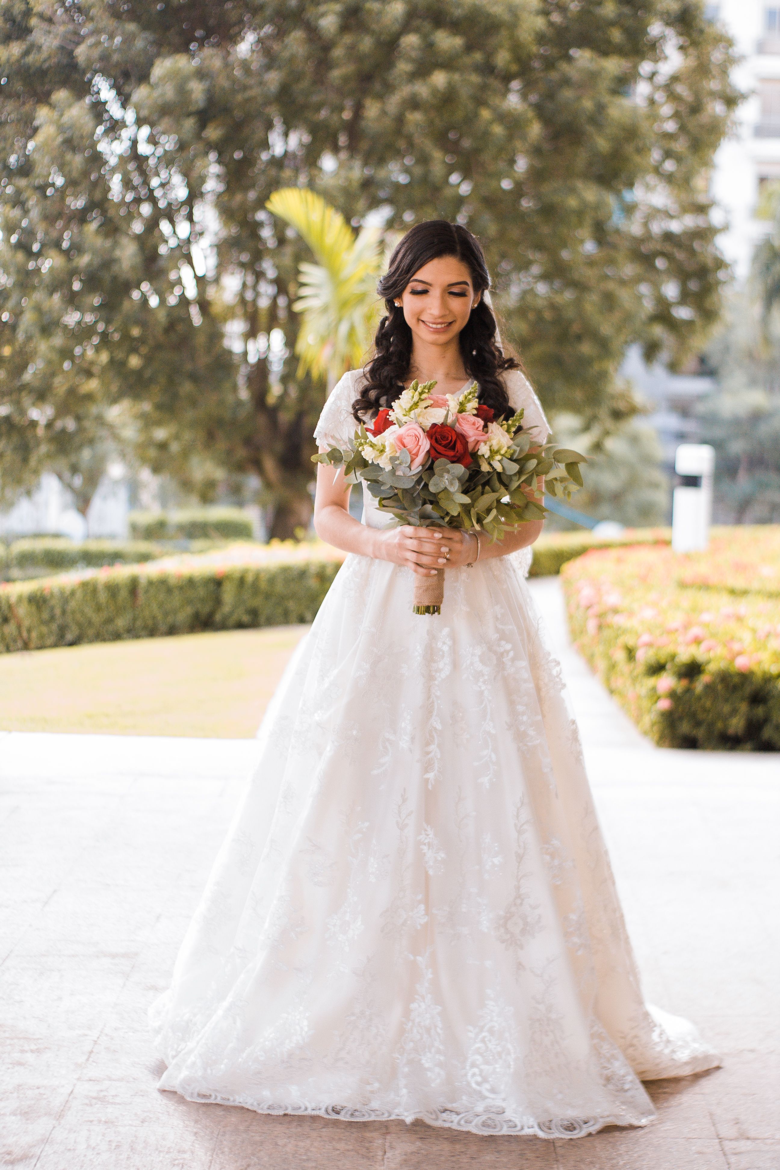A beautiful bride in a white gown holding a bouquet outdoors in a lush garden setting.