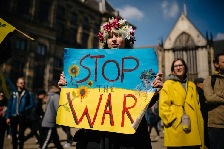 Woman In A Flower Garland And Bloody Makeup Holding A Stop The War Banner Standing In The City Square