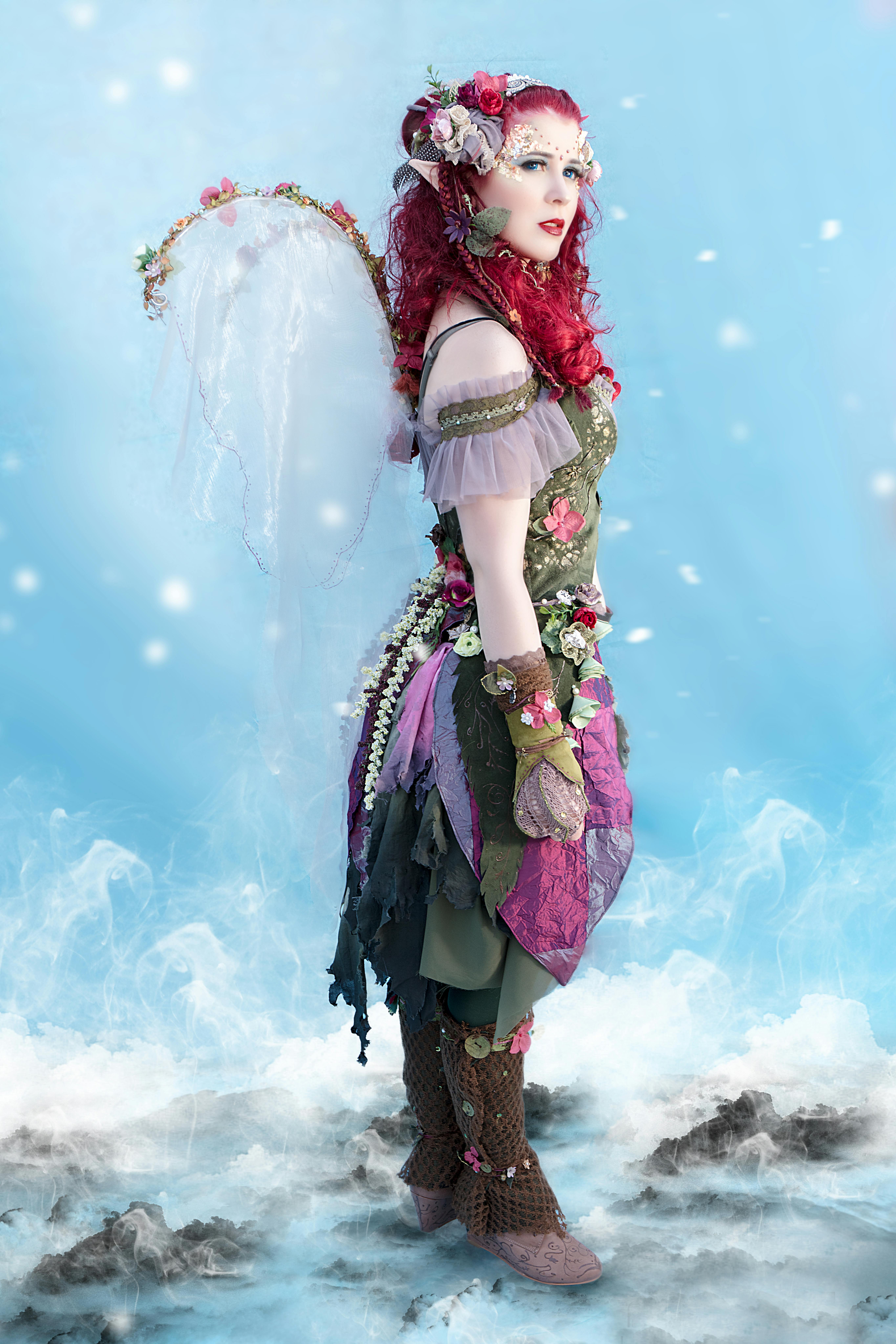 Red-haired woman in fairy costume with wings in a whimsical, snowy fantasy setting.