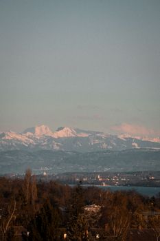 Serene landscape of snow-capped mountains with a river and forest at sunset, capturing winter's beauty.