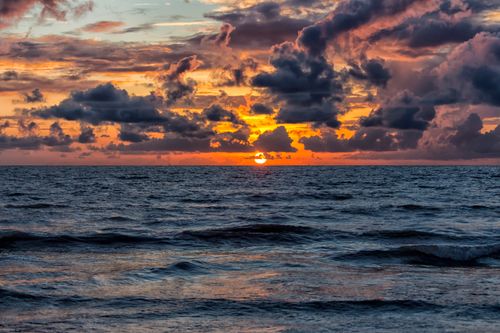 Free Vibrant sunset over the ocean with dramatic clouds creating a picturesque view. Stock Photo