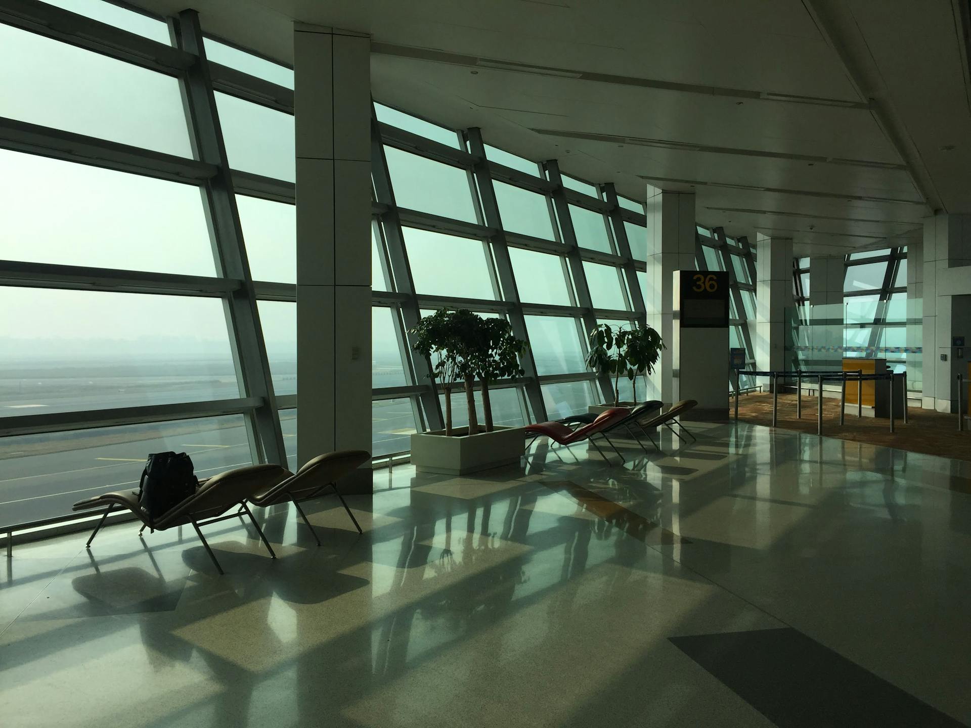 Sunlit empty terminal at New Delhi Airport with chairs and large windows.