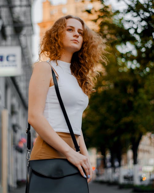 Wanita Dengan Atasan Tanpa Lengan Turtleneck Putih Dan Bawahan Coklat Memegang Pakaian Tas Selempang Kulit Hitam
