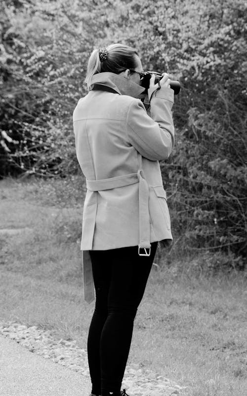 Grayscale Photo of a Woman in a Coat Using a Camera