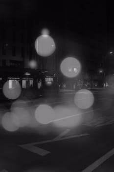 Atmospheric black and white city street with tram and bokeh lights at night.