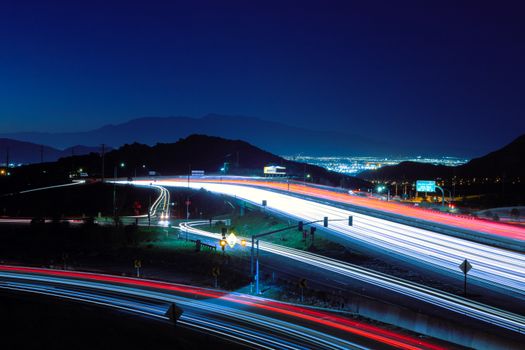 Dynamic light trails on the highway in Riverside, CA with mountain backdrop at night.