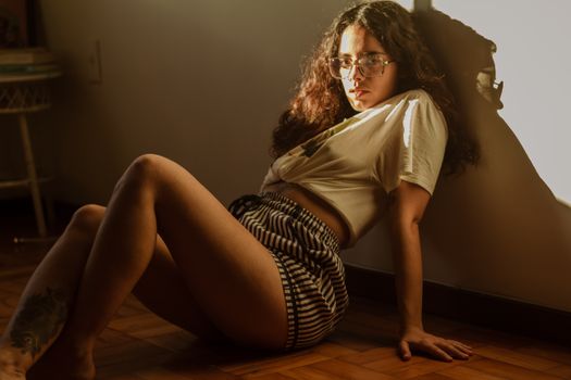 Woman sitting indoors in warm lighting, wearing eyeglasses and striped shorts.