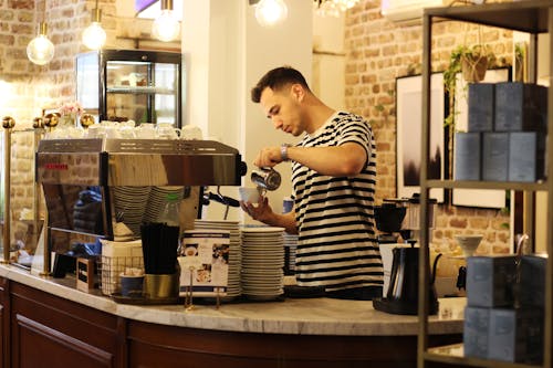 Photograph of a Man in a Striped Shirt Pouring Coffee into a Cup