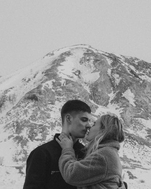 Grayscale Photo of a Couple Kissing Near a Mountain