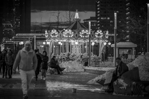 Grayscale Photo of People Walking Near a Carousel