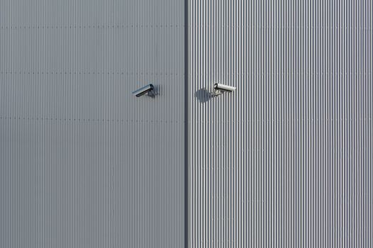 Corrugated metal wall with two mounted security cameras in a minimalist style.