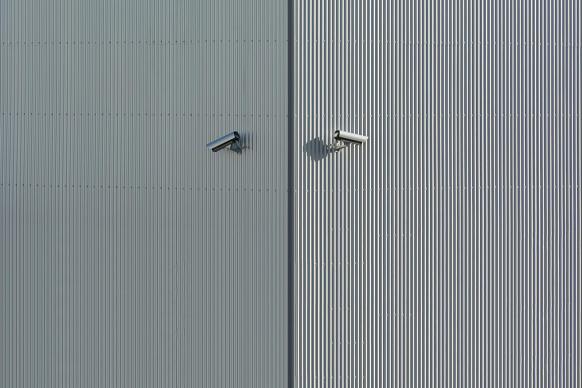 Corrugated metal wall with two mounted security cameras in a minimalist style.