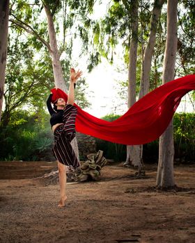 Woman dancing with a red scarf in a tranquil forest, embodying elegance and movement.