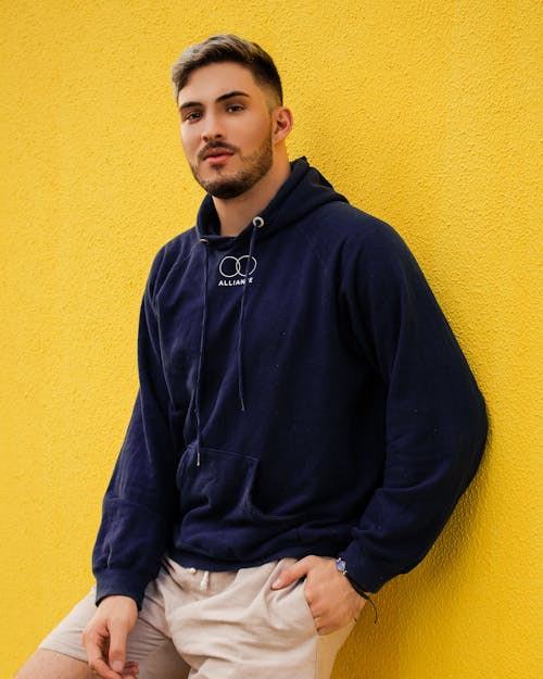 Man in a Blue Hoodie Leaning on a Yellow Wall
