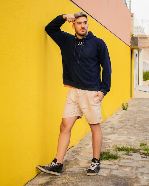 Man in a Blue Hoodie Posing Beside a Yellow Wall