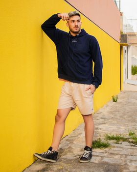 Young adult posing against vibrant yellow wall in casual outfit.