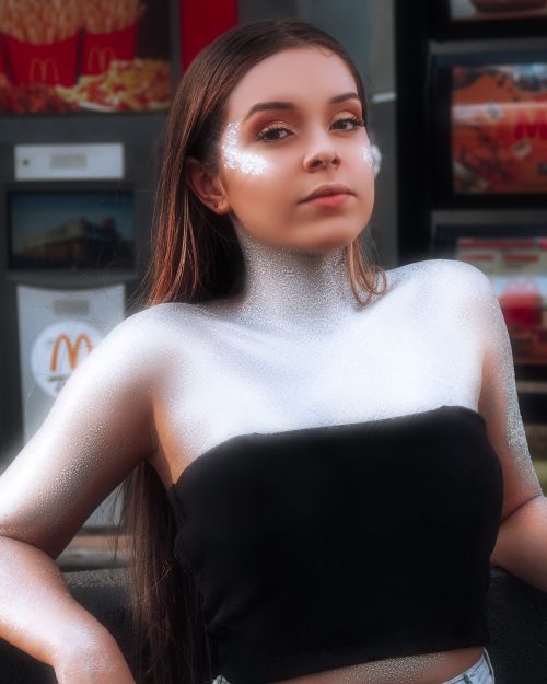 Free Portrait of a teenager in glitter makeup posing confidently at an urban location with a vending machine backdrop. Stock Photo