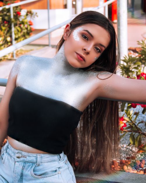 Free A stunning portrait of a young woman with silver glitter on her face and neck, posing outdoors. Stock Photo