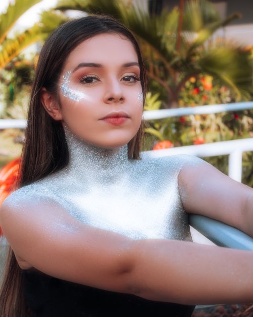 Free A young woman with glitter on her face and shoulders, posing outdoors surrounded by greenery. Stock Photo