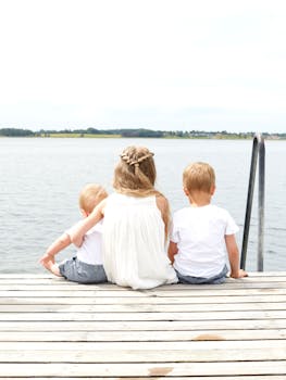 三个孩子坐在湖边宁静的木码头上，构成一幅夏日的宁静景象