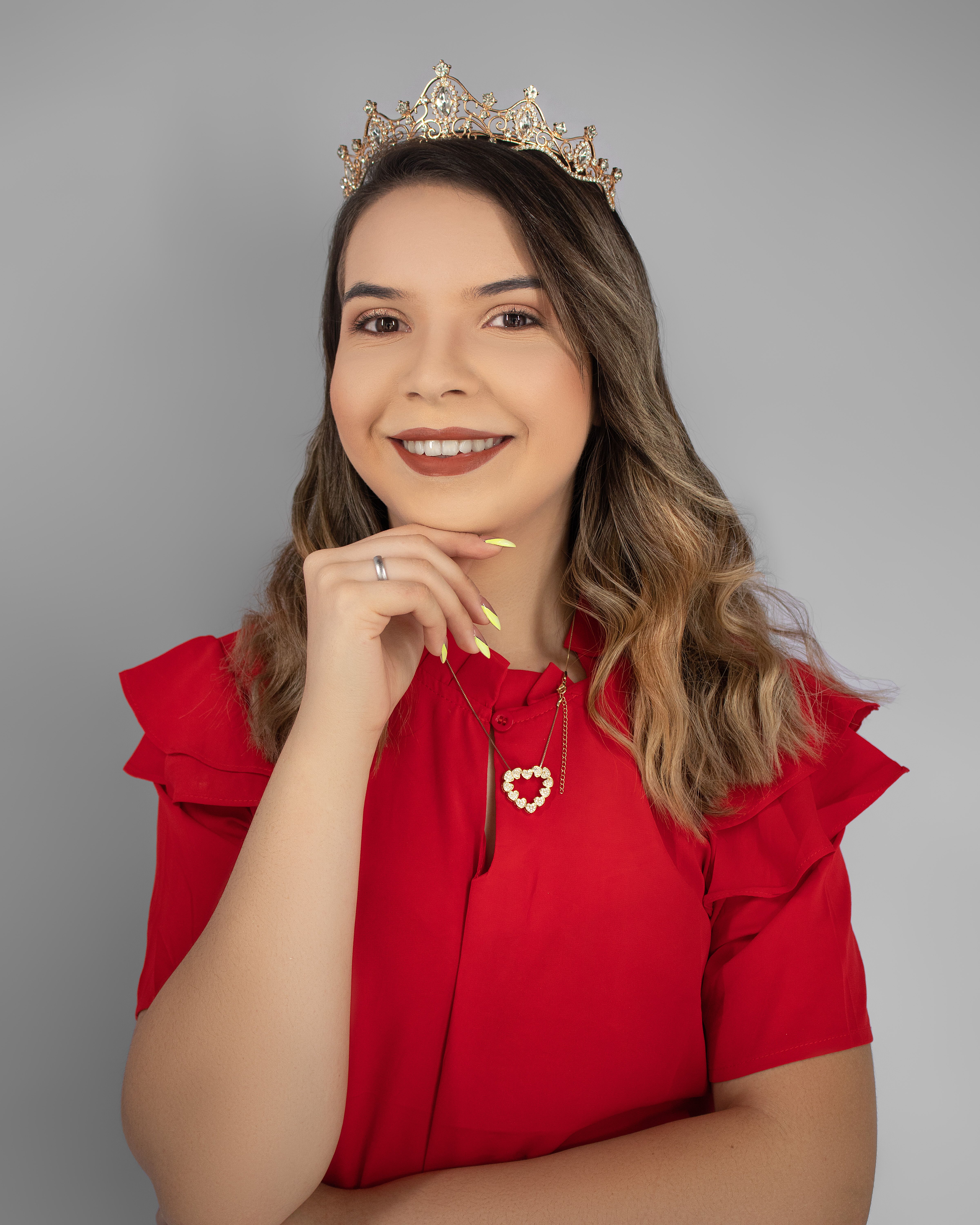 Portrait of a smiling woman in a red dress and tiara, hand on chin, in a studio setting.
