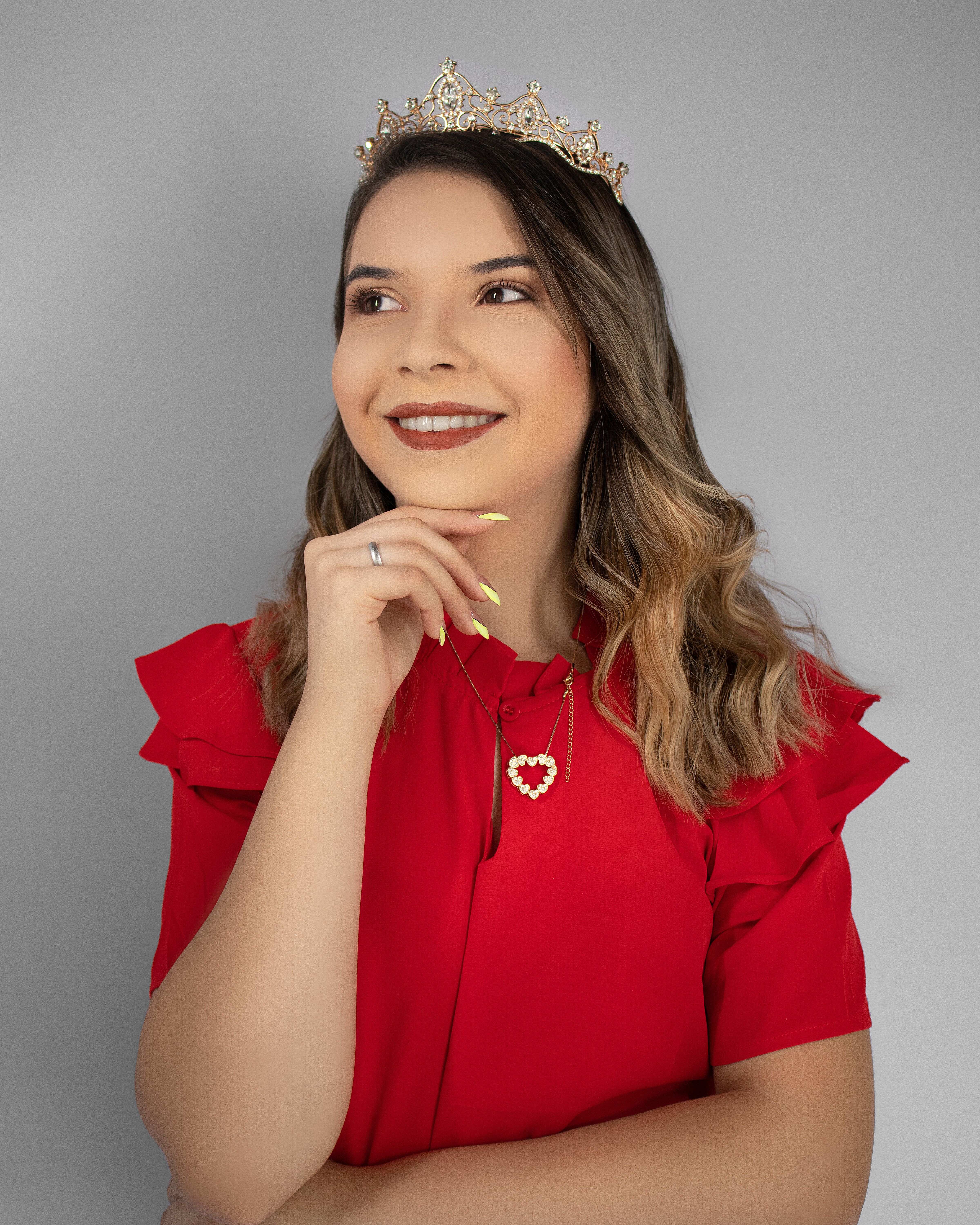 Portrait of a smiling woman in a red blouse and crown, exuding confidence and elegance.