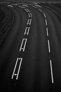 Grayscale aerial shot of a curved road with lane markings, showing abstract lines.