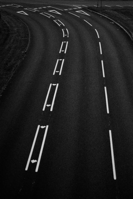 Grayscale aerial shot of a curved road with lane markings, showing abstract lines.