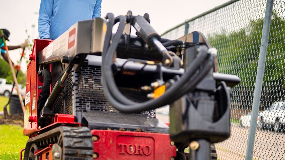 A worker operating a trenching machine across a grass field