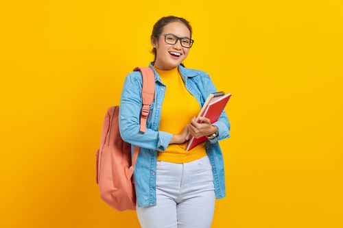 Free Cheerful student in denim and backpack holding notebooks against a yellow background. Stock Photo