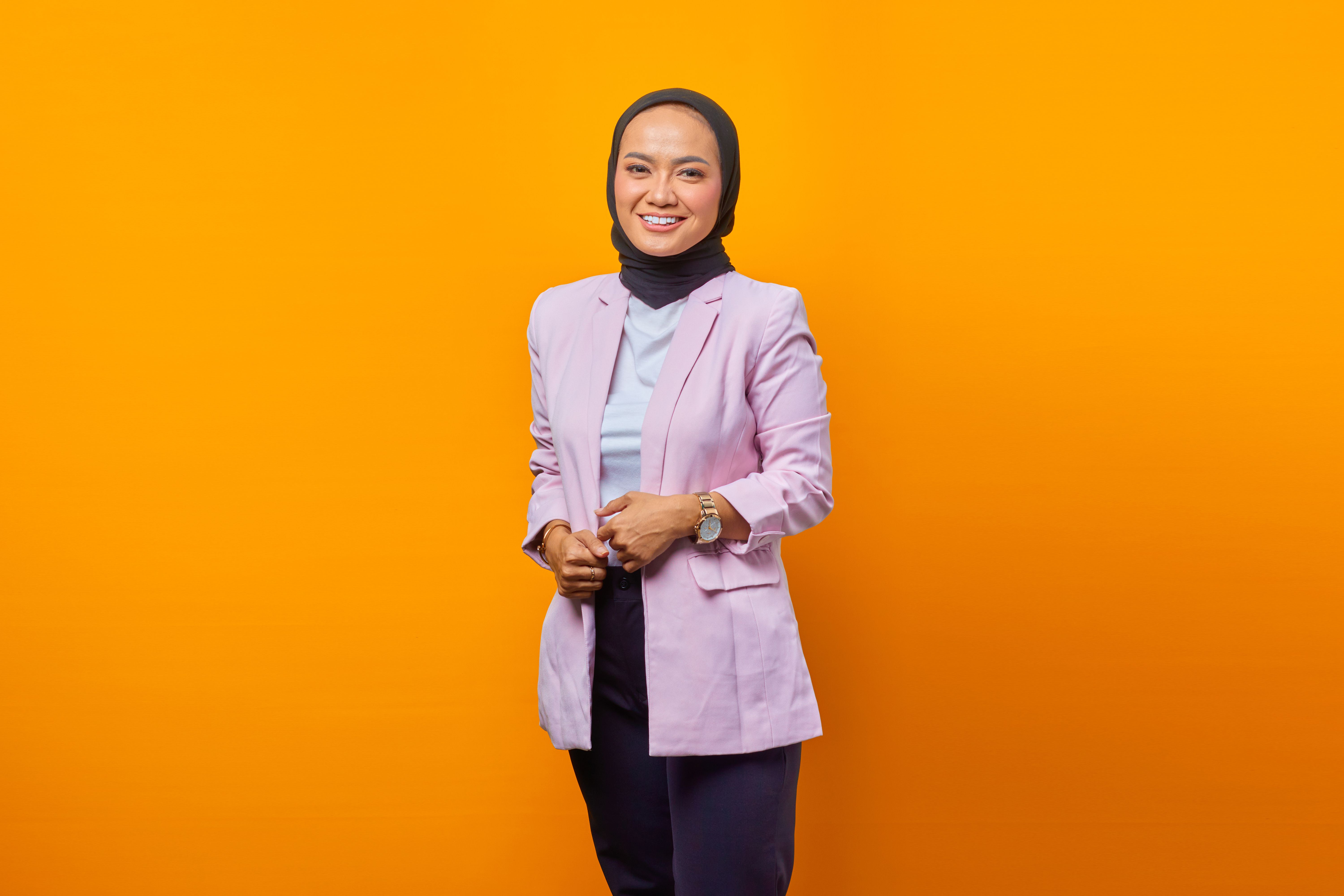 Fashionable woman in hijab against orange background, exuding confidence and style.