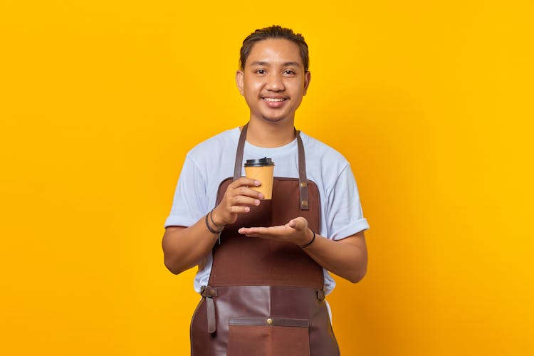 A Man Wearing Brown Apron Holding A Brown Disposable Coffee Cup