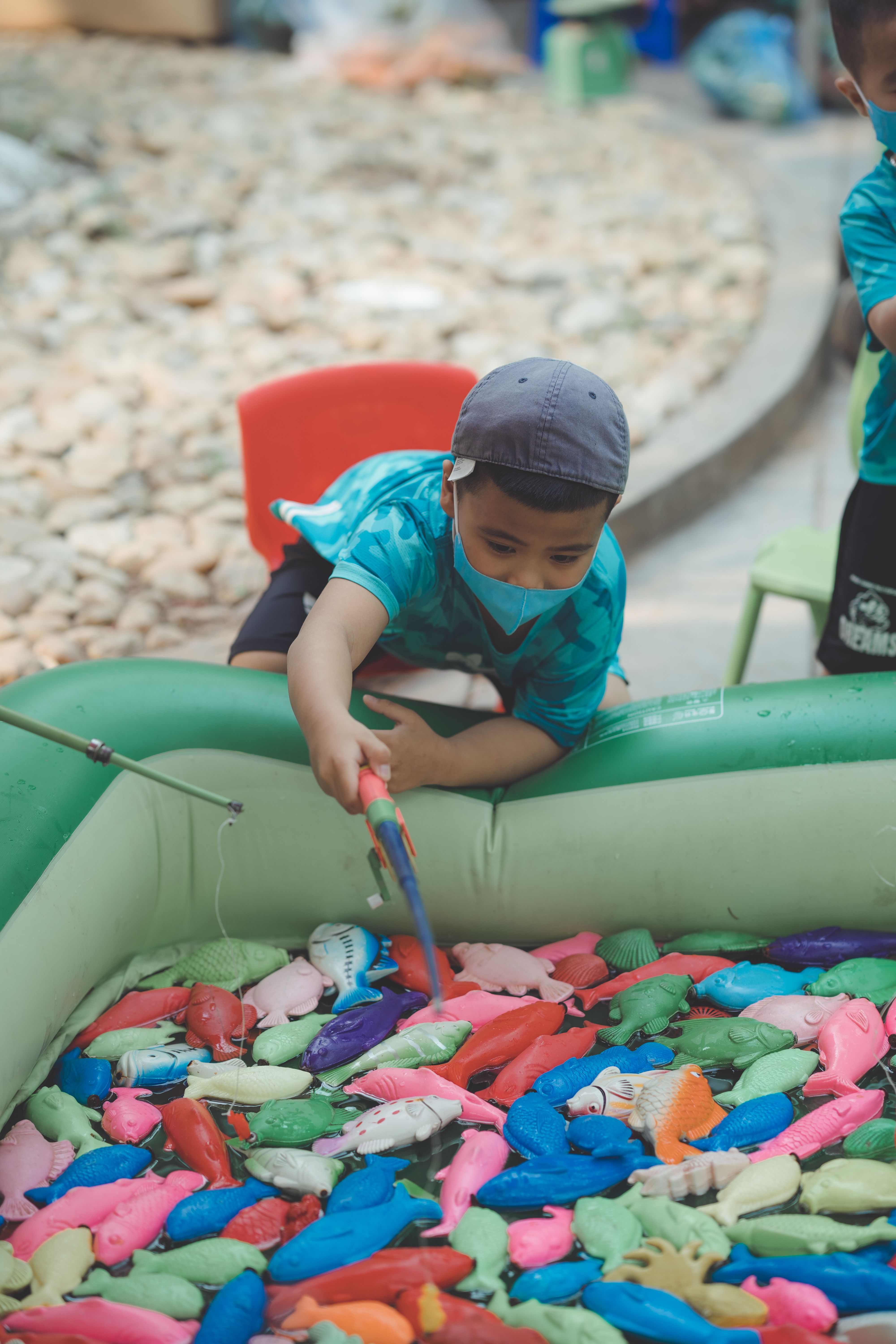 A young boy enjoys a playful moment fishing for toy fish in an inflatable pool outdoors.