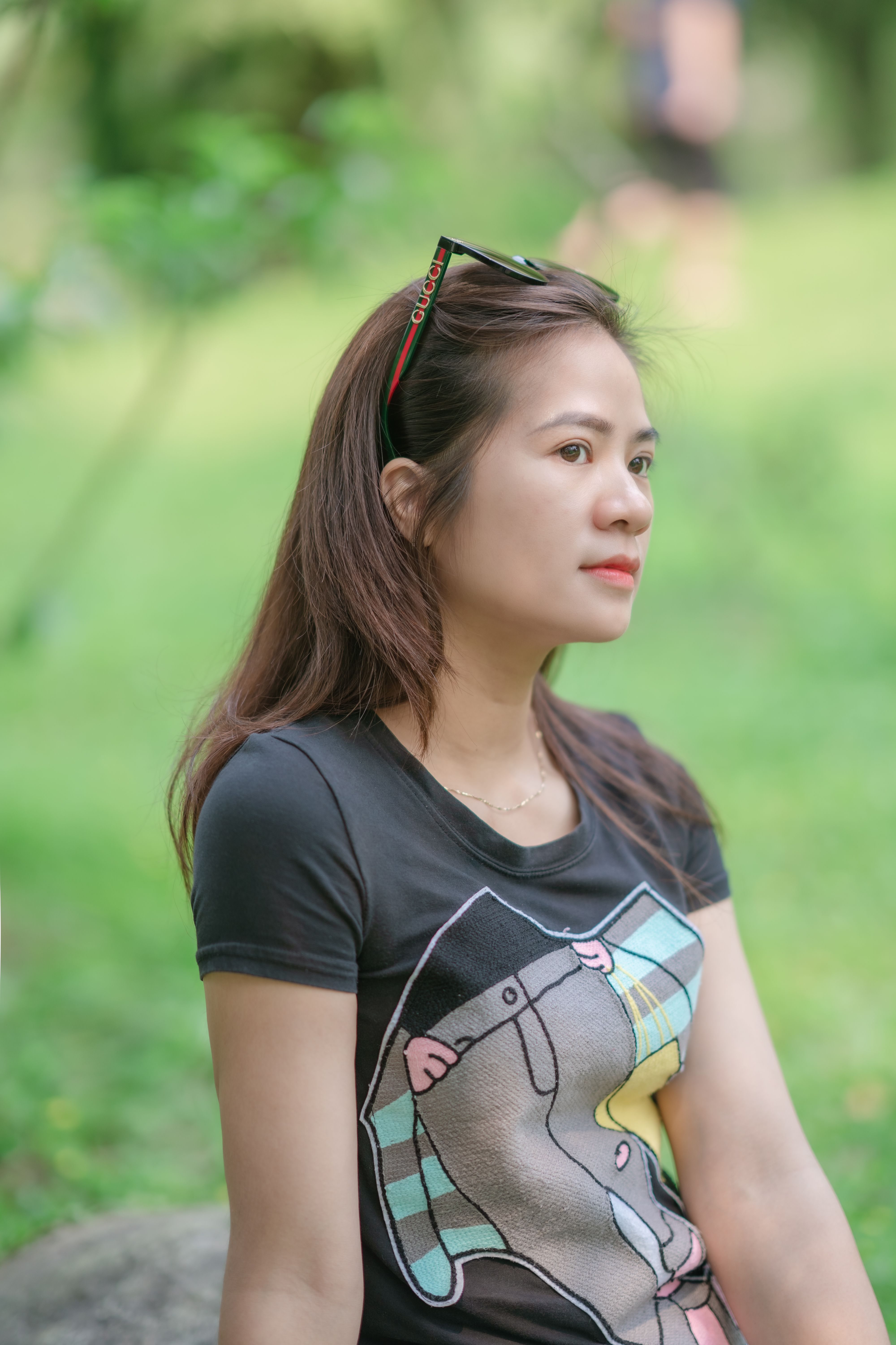 Young woman sitting outdoors in summer, wearing a graphic t-shirt and sunglasses, enjoying the tranquility.