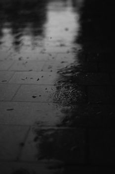 Black and white photo of raindrops on wet pavement, creating a somber mood.