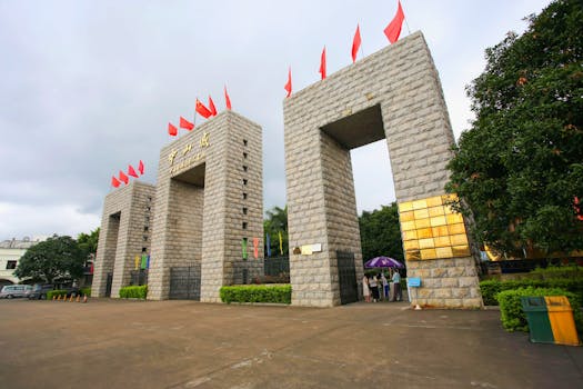Entrance gate with red flags and Chinese script under cloudy sky, showcasing cultural architecture.