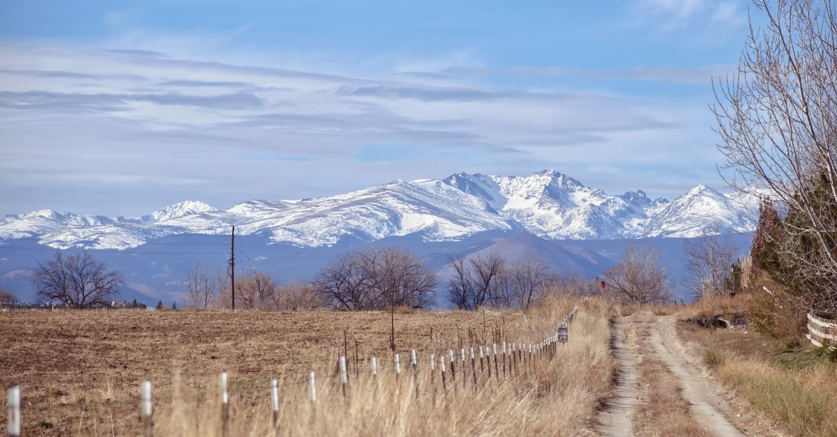 Explore the serene beauty of a countryside dirt road with snowy mountain views under a clear blue sky.